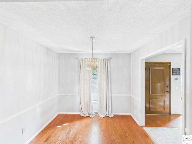 unfurnished dining area with wood finished floors, a textured ceiling, and baseboards
