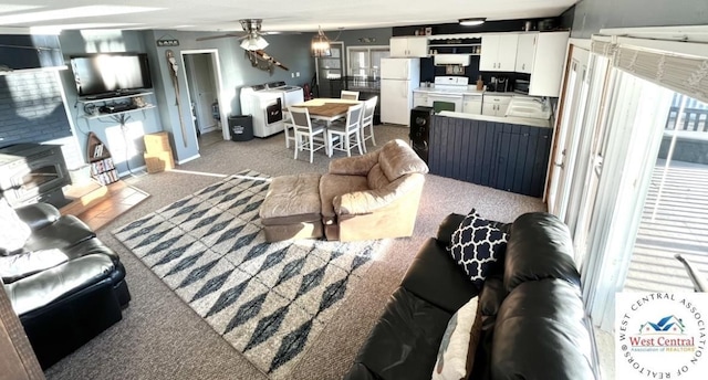 living area with a wood stove, carpet flooring, ceiling fan, baseboards, and washer and dryer