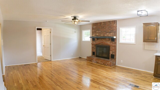 1903 E Alfresco St, Clinton, MO 64735 - unfurnished living room with a ceiling fan, light wood-style floors, a brick fireplace, and a textured ceiling