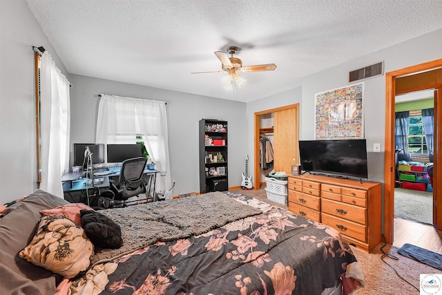 bedroom featuring a textured ceiling, an office area, ceiling fan, a closet, and wood finished floors