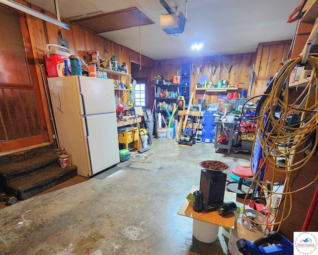 garage featuring freestanding refrigerator, a garage door opener, wood walls, and a workshop area