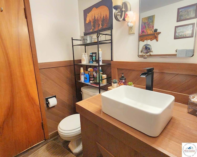 half bath with a sink, toilet, a wainscoted wall, and wood walls