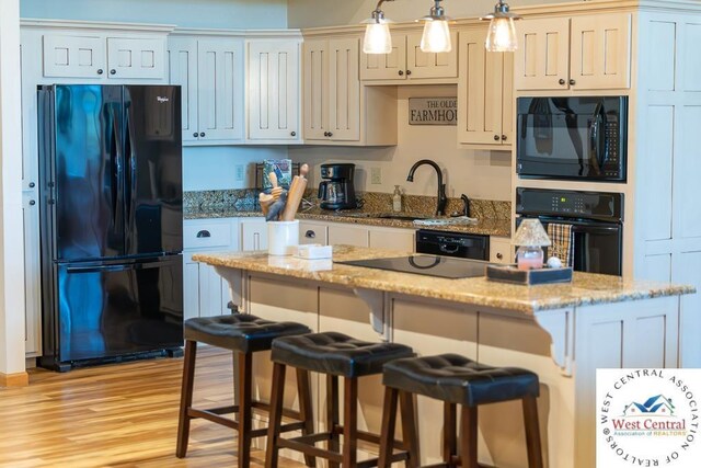 662 W 6th St, Schell City, MO 64783 - kitchen featuring black appliances, a sink, a kitchen bar, light wood-type flooring, and a kitchen island