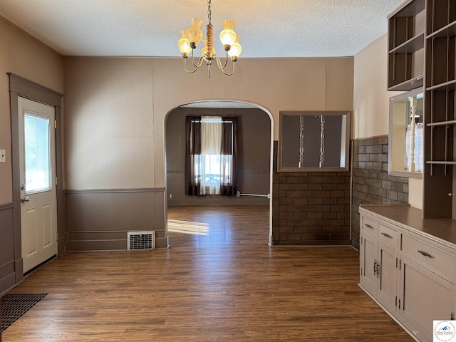 unfurnished dining area with a textured ceiling, visible vents, arched walkways, dark wood-type flooring, and a notable chandelier