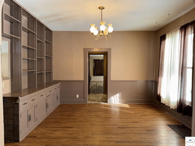 unfurnished dining area featuring an inviting chandelier, visible vents, a textured ceiling, wainscoting, and wood finished floors