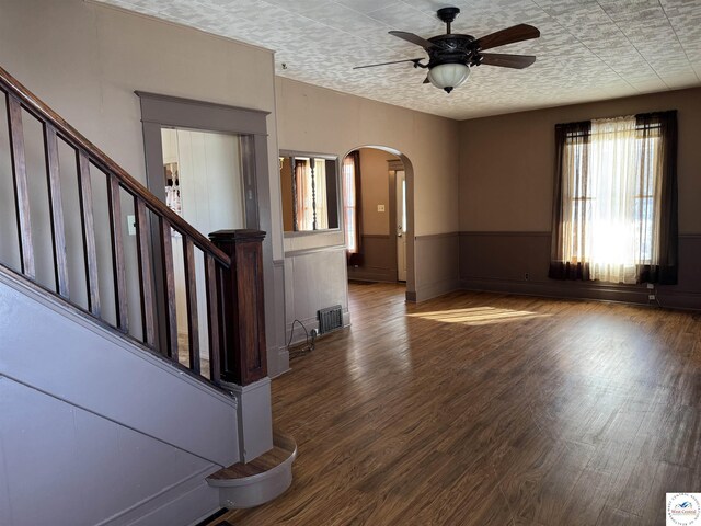 interior space with arched walkways, wood finished floors, wainscoting, ceiling fan, and stairway