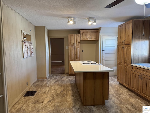kitchen featuring brown cabinets, stovetop, visible vents, baseboards, and wooden walls