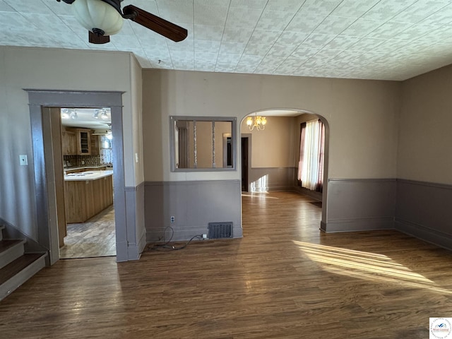 unfurnished room featuring a wainscoted wall, a ceiling fan, visible vents, arched walkways, and wood finished floors