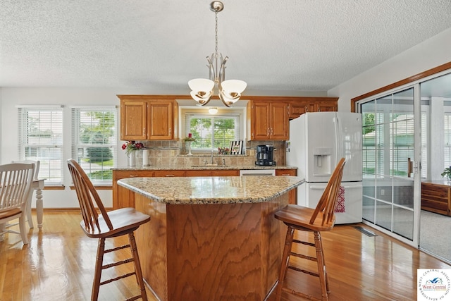 1515 NW Primrose Ln, Blue Springs, MO 64015 - kitchen featuring white refrigerator with ice dispenser, a textured ceiling, light wood finished floors, a breakfast bar area, and a chandelier