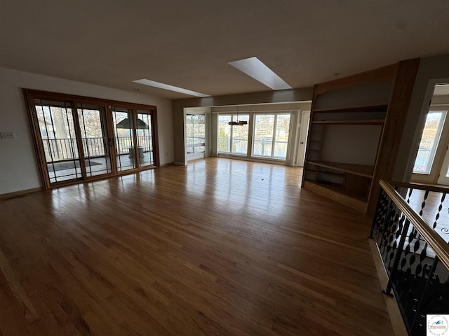 unfurnished living room with baseboards, a skylight, and wood finished floors