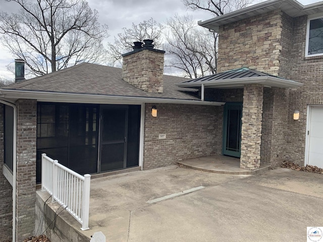 property entrance featuring a chimney, brick siding, a standing seam roof, a patio, and roof with shingles