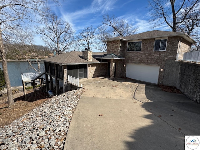 tri-level home featuring driveway, a chimney, a sunroom, brick siding, and a garage
