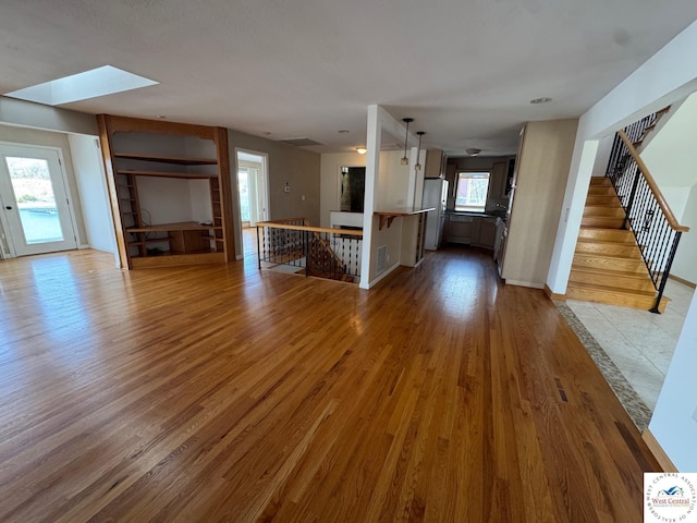 unfurnished living room with light wood-style floors, visible vents, and a skylight