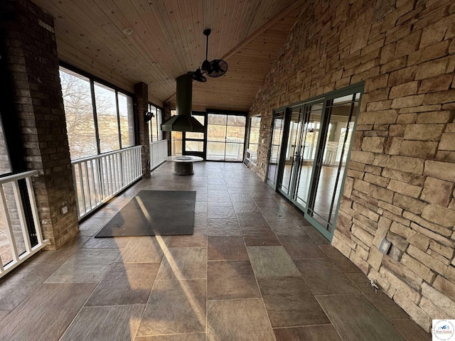 unfurnished sunroom featuring wood ceiling, stone finish floor, and high vaulted ceiling