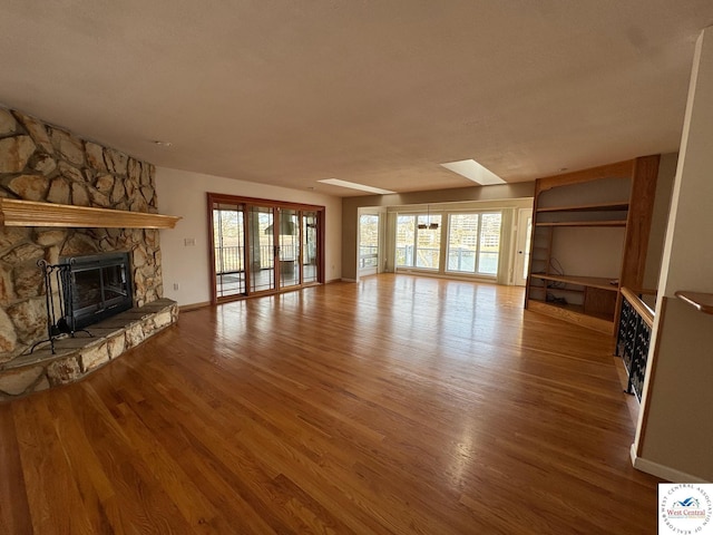 unfurnished living room featuring a skylight, a stone fireplace, wood finished floors, and baseboards