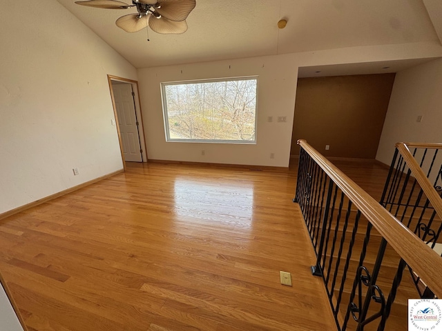 empty room featuring lofted ceiling, light wood-type flooring, a ceiling fan, and baseboards
