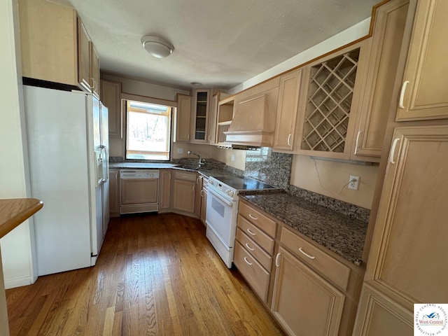 kitchen featuring wood finished floors, white appliances, glass insert cabinets, dark stone counters, and custom range hood