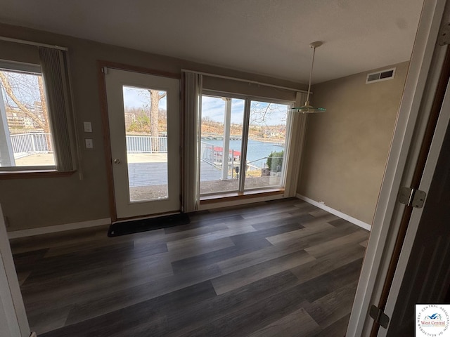 unfurnished dining area featuring dark wood-style flooring, visible vents, plenty of natural light, and baseboards
