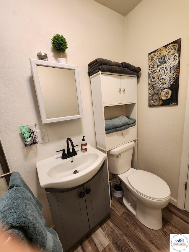 half bathroom featuring wood finished floors, toilet, and vanity