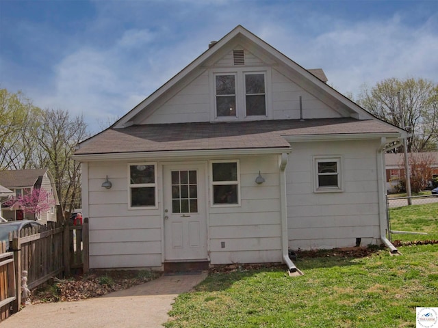 back of house featuring fence, a yard, and a shingled roof