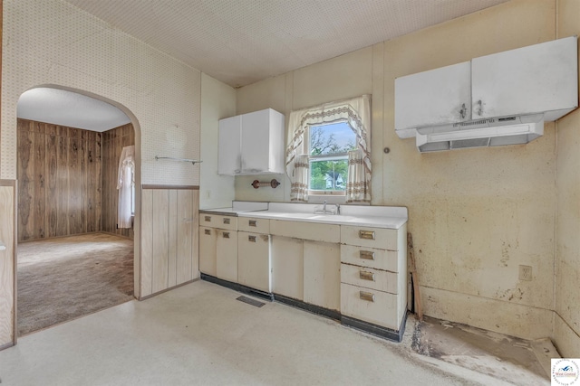 kitchen featuring visible vents, wooden walls, light countertops, a wainscoted wall, and arched walkways