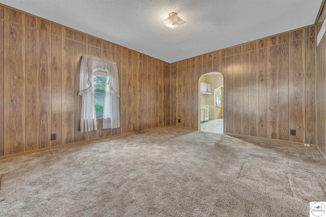 unfurnished room with arched walkways, a textured ceiling, carpet flooring, and wood walls