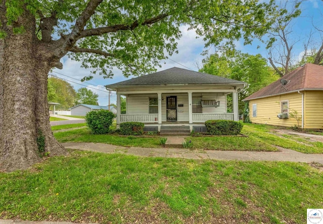 view of front of property featuring roof with shingles, covered porch, and a front lawn