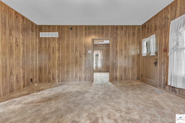 carpeted spare room with visible vents, wood walls, and a textured ceiling