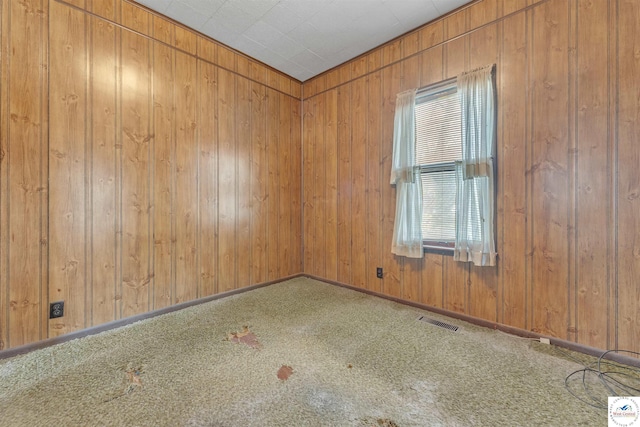 carpeted spare room with visible vents and wood walls