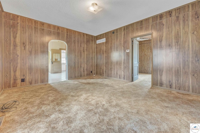 empty room featuring carpet floors, arched walkways, wood walls, and visible vents