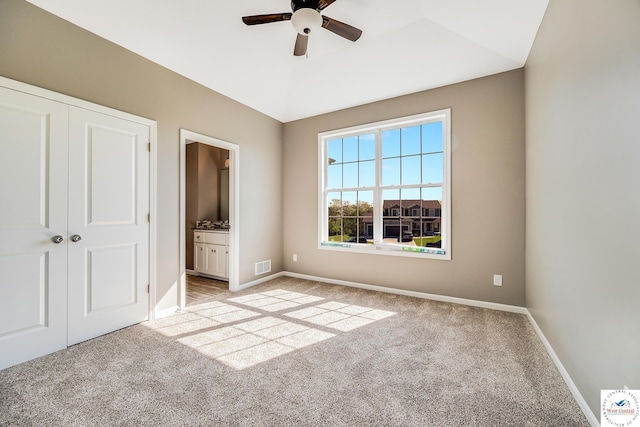 unfurnished bedroom with light carpet, baseboards, ensuite bath, a closet, and a ceiling fan