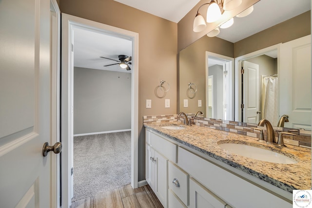 full bathroom featuring ceiling fan, wood finished floors, double vanity, baseboards, and a chandelier