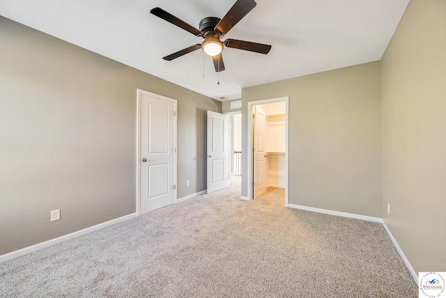 unfurnished bedroom with carpet, baseboards, a walk in closet, and ceiling fan