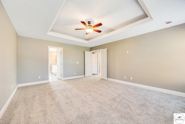 unfurnished bedroom with a tray ceiling, light carpet, baseboards, ensuite bathroom, and crown molding