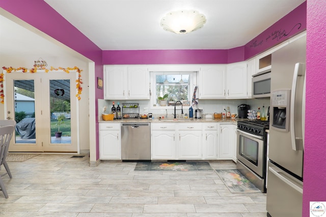 kitchen with white cabinetry, a sink, stainless steel appliances, light countertops, and light wood finished floors