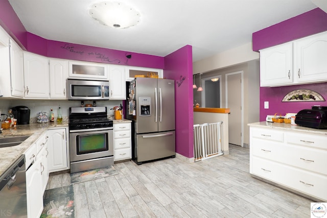 kitchen with light stone countertops, appliances with stainless steel finishes, white cabinets, a sink, and light wood-type flooring