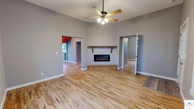 unfurnished living room with a glass covered fireplace, light wood-style floors, ceiling fan, and baseboards