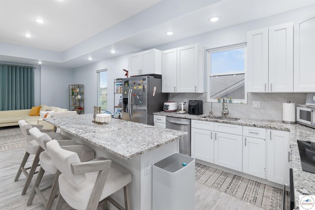 kitchen featuring white cabinetry, a sink, stainless steel appliances, a center island, and a kitchen bar