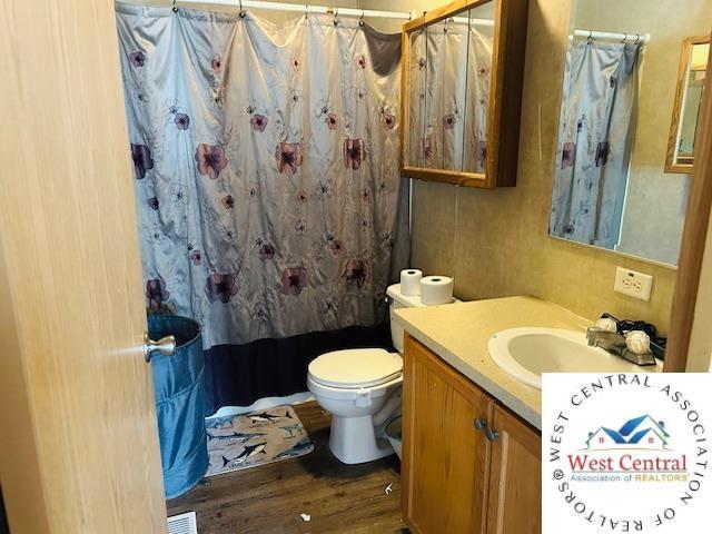 214 SE State St, Milan, MO 63556 - bathroom featuring wood finished floors, a shower with shower curtain, toilet, vanity, and visible vents