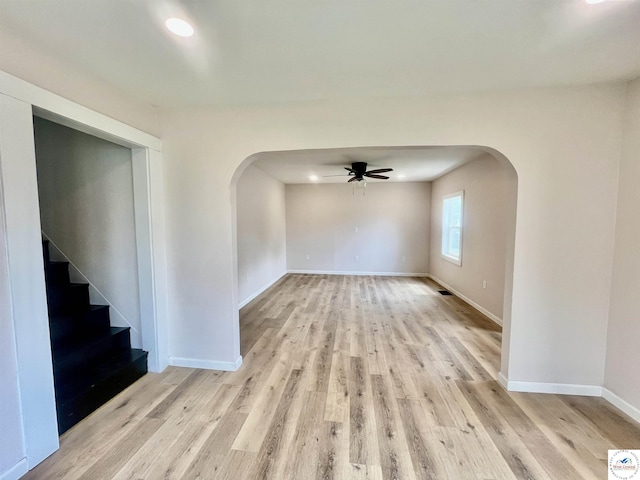 spare room featuring arched walkways, baseboards, a ceiling fan, and light wood-style flooring