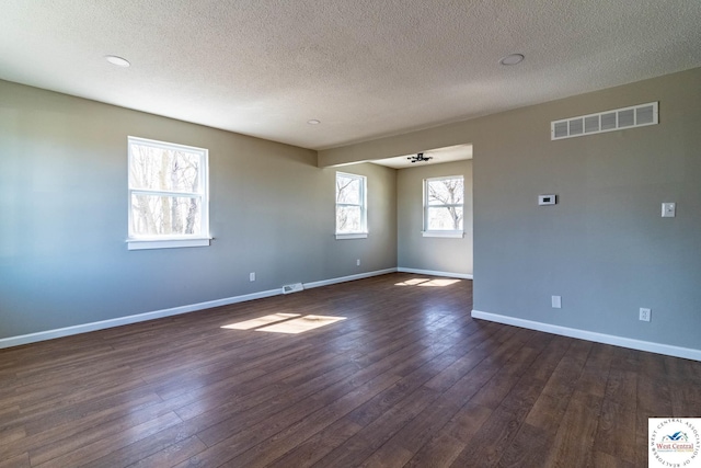 spare room featuring dark wood-type flooring, a textured ceiling, visible vents, and baseboards