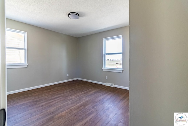 spare room featuring dark wood-style flooring, visible vents, a textured ceiling, and baseboards