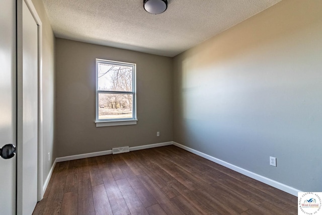 empty room featuring dark wood-style floors, a textured ceiling, visible vents, and baseboards