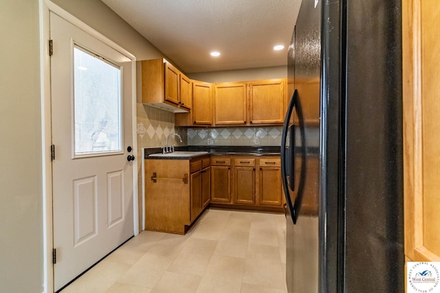 kitchen with brown cabinets, a sink, decorative backsplash, dark countertops, and freestanding refrigerator