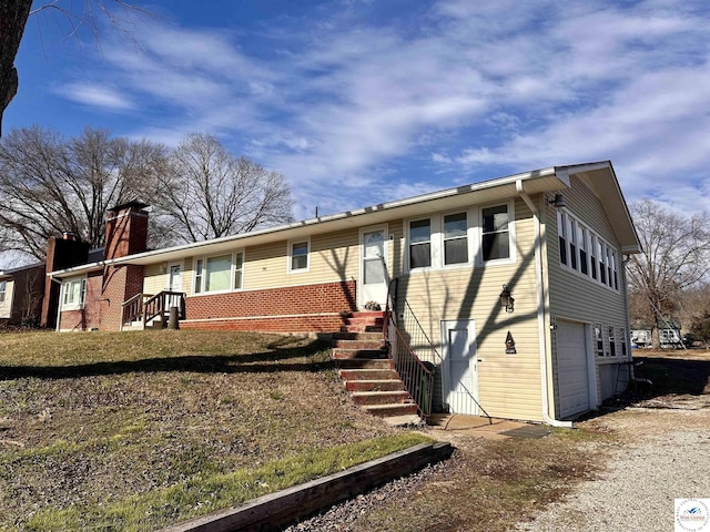 back of house with driveway, a chimney, brick siding, and a garage