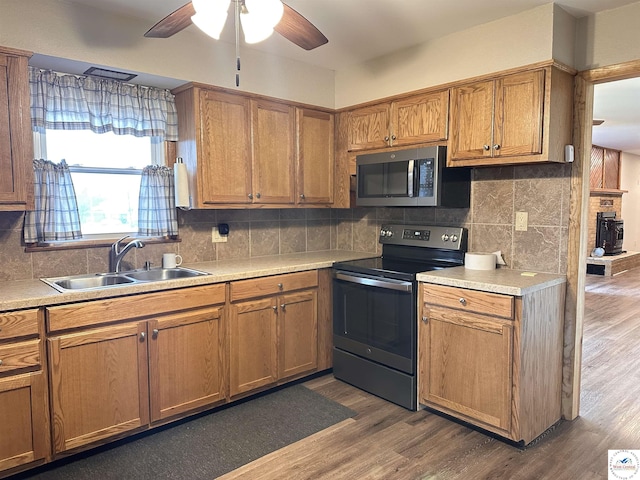 kitchen featuring dark wood-style floors, a sink, ceiling fan, brown cabinetry, and appliances with stainless steel finishes