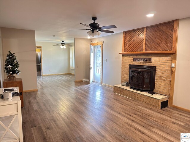 unfurnished living room featuring a wood stove, a ceiling fan, wood finished floors, and baseboards