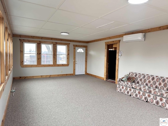 unfurnished living room featuring baseboards, a drop ceiling, carpet floors, and an AC wall unit