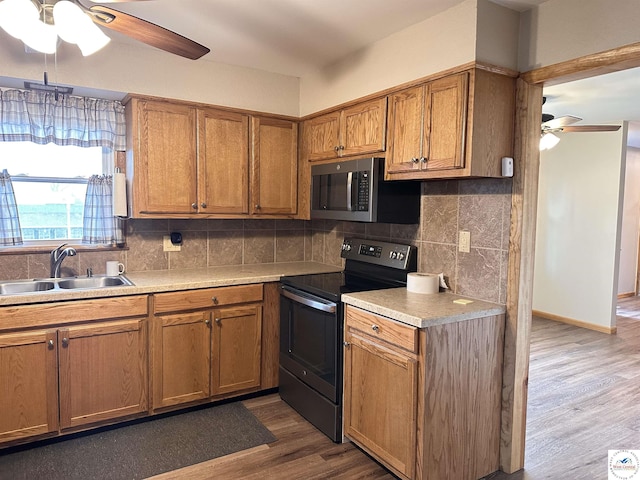 kitchen featuring brown cabinets, a sink, ceiling fan, stainless steel appliances, and wood finished floors