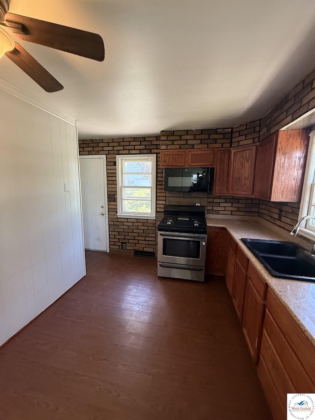 7801 Ozark Rd, Kansas City, MO 64129 - kitchen with black microwave, stainless steel range with gas stovetop, light countertops, a ceiling fan, and brown cabinetry